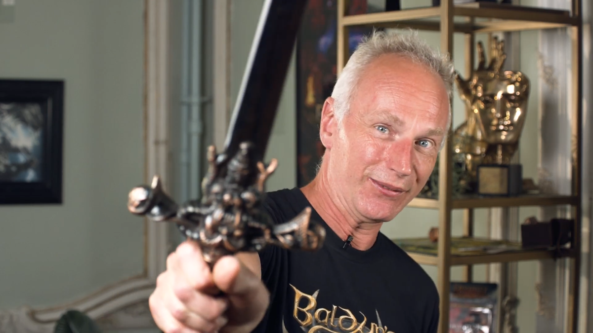 Larian CEO Swen Vincke brandishes a sword at the camera and smiles.